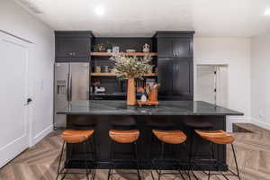 Kitchen with a breakfast bar, a large island, stainless steel refrigerator with ice dispenser, parquet floors, and dark stone countertops