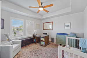 Bedroom featuring a crib, ceiling fan, and a raised ceiling