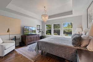 Bedroom with a notable chandelier, a raised ceiling, dark hardwood / wood-style floors, and a textured ceiling