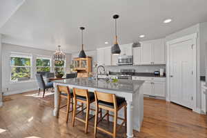 Kitchen with an island with sink, white cabinetry, wood-type flooring, and stainless steel appliances