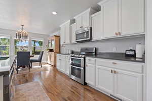 Kitchen with appliances with stainless steel finishes, hanging light fixtures, white cabinets, a textured ceiling, and wood-type flooring