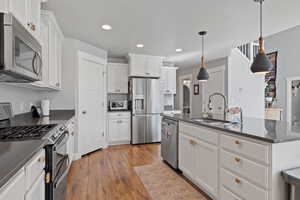 Kitchen with pendant lighting, white cabinets, sink, light hardwood / wood-style flooring, and stainless steel appliances