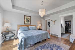 Bedroom with a tray ceiling, an inviting chandelier, and hardwood / wood-style flooring