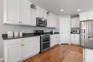 Kitchen with appliances with stainless steel finishes, wood-type flooring, and white cabinetry