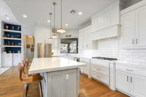 Kitchen featuring white cabinets, decorative light fixtures, appliances with stainless steel finishes, a center island, and light hardwood / wood-style floors