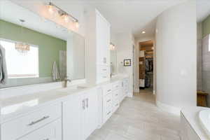 Bathroom featuring tiled tub, vanity, a chandelier, and tile patterned floors