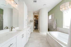 Bathroom featuring a notable chandelier, vanity, tile patterned floors, and a relaxing tiled tub