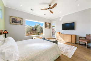 Bedroom with ceiling fan, light wood-type flooring, and ornamental molding