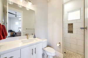 Bathroom featuring ceiling fan, vanity, a tile shower, toilet, and a wealth of natural light