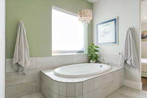 Bathroom with tiled bath, a chandelier, and tile patterned floors