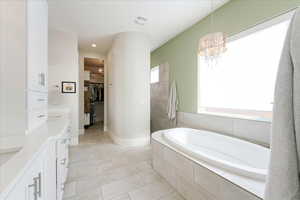 Bathroom with a wealth of natural light, a chandelier, tiled tub, and vanity