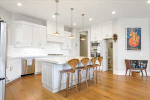 Kitchen with appliances with stainless steel finishes, light hardwood / wood-style floors, white cabinets, a barn door, and a center island