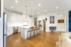 Kitchen featuring light hardwood / wood-style floors, white cabinetry, hanging light fixtures, a kitchen island, and stainless steel appliances