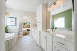 Bathroom featuring ceiling fan with notable chandelier, tiled tub, vanity, and tile patterned floors