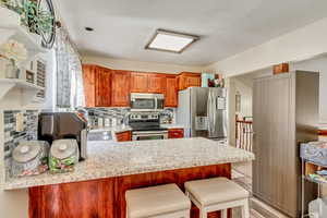 Kitchen with appliances with stainless steel finishes, light hardwood / wood-style floors, tasteful backsplash, kitchen peninsula, and a kitchen bar