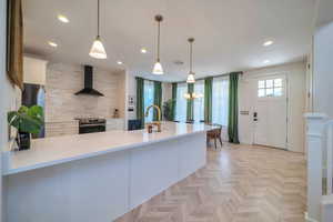 Kitchen with sink, hanging light fixtures, wall chimney range hood, decorative backsplash, and appliances with stainless steel finishes