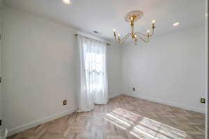 Spare room featuring a chandelier, light parquet floors, and crown molding