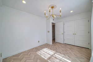 Unfurnished bedroom with a closet, a chandelier, ornamental molding, and light parquet flooring