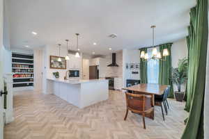 Kitchen featuring pendant lighting, kitchen peninsula, wall chimney exhaust hood, white cabinetry, and appliances with stainless steel finishes