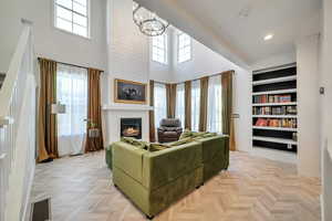 Living room with light parquet flooring, a high ceiling, a chandelier, and plenty of natural light