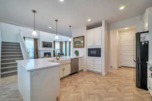 Kitchen featuring pendant lighting, sink, white cabinetry, stainless steel appliances, and light parquet flooring