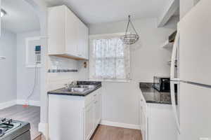 Kitchen with light wood-type flooring, white refrigerator, white cabinetry, hanging light fixtures, and decorative backsplash