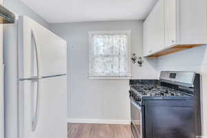 Kitchen featuring white cabinets, light hardwood / wood-style floors, white refrigerator, and gas range