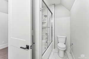 Bathroom featuring enclosed tub / shower combo, lofted ceiling, and toilet