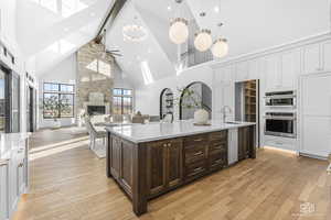 Kitchen with sink, a large fireplace, an island with sink, dark brown cabinetry, and high vaulted ceiling