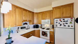 Kitchen with light hardwood / wood-style flooring, white appliances, kitchen peninsula, and sink