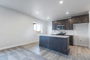 Kitchen with gas stove, light hardwood / wood-style flooring, a kitchen island with sink, and sink