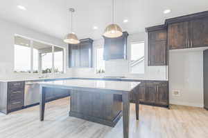 Kitchen with stainless steel dishwasher, custom range hood, pendant lighting, light hardwood / wood-style floors, and a center island