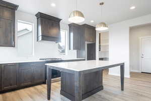 Kitchen with hanging light fixtures, custom range hood, stainless steel stove, a center island, and light hardwood / wood-style floors