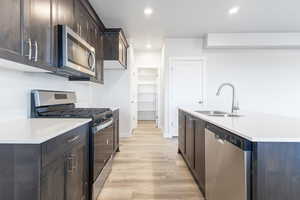 Kitchen with appliances with stainless steel finishes, sink, light wood-type flooring, dark brown cabinetry, and a center island with sink