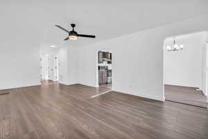 Unfurnished living room with ceiling fan with notable chandelier and hardwood / wood-style floors