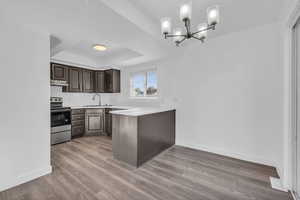 Kitchen with a raised ceiling, dark brown cabinets, electric range, and hardwood / wood-style flooring