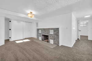 Unfurnished living room with carpet, a tiled fireplace, and a textured ceiling