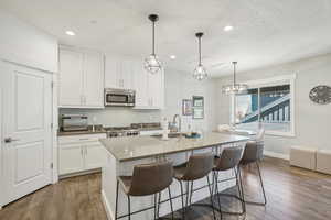 Kitchen featuring hanging light fixtures, white cabinetry, stainless steel appliances, a center island with sink, and dark hardwood / wood-style floors