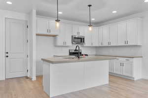 Kitchen with pendant lighting, a center island with sink, appliances with stainless steel finishes, and white cabinetry