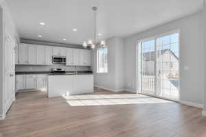 Kitchen with hanging light fixtures, white cabinetry, a kitchen island with sink, light hardwood / wood-style flooring, and stainless steel appliances