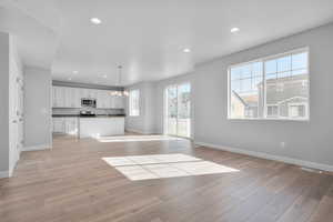 Unfurnished living room with sink, light hardwood / wood-style floors, a notable chandelier, and a healthy amount of sunlight