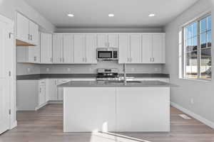 Kitchen featuring a kitchen island with sink, white cabinetry, stainless steel appliances, and light hardwood / wood-style floors