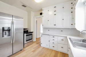 Kitchen with white cabinets, appliances with stainless steel finishes, sink, and light hardwood / wood-style flooring