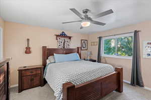 Bedroom featuring ceiling fan, light colored carpet, and a textured ceiling