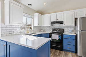 Kitchen with sink, vaulted ceiling, black electric range oven, blue cabinets, and stainless steel fridge