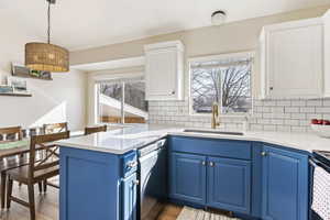 Kitchen with blue cabinets, sink, white dishwasher, and plenty of natural light