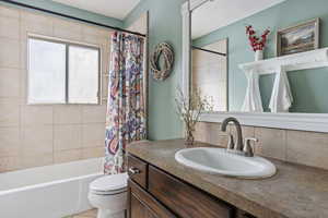 Full bathroom with shower / bath combo, backsplash, tile patterned floors, vanity, and toilet