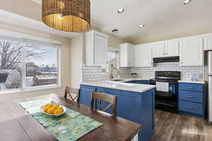 Kitchen with black range with electric stovetop, white cabinets, blue cabinets, backsplash, and dark hardwood / wood-style floors