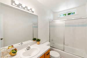 Full bathroom upstairs with enclosed tub/shower combo, vanity, and toilet