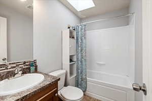 Full bathroom with shower / bath combination with curtain, tasteful backsplash, a skylight, vanity, and toilet